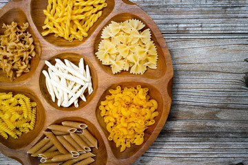 Various mix of pasta and small red tomatoes on wooden bowl