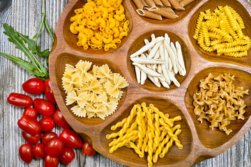 Various mix of pasta and small red tomatoes on wooden bowl
