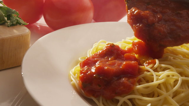 Pouring marinara sauce onto spaghetti