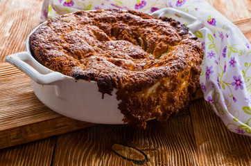 Apple pie in a white baking dish on the wooden background.