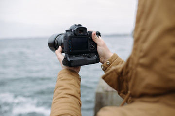 Unrecognizable man holding a camera and shooting sea wave