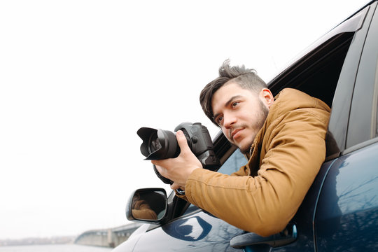 Handsome man with camera photoshooting from car