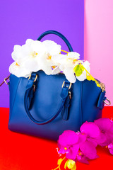 blue fashionable female bag with flowers orchid on a bright background