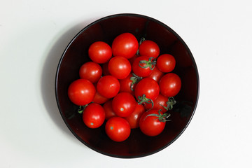 несколько маленьких помидоров в черной тарелки на белом фоне
