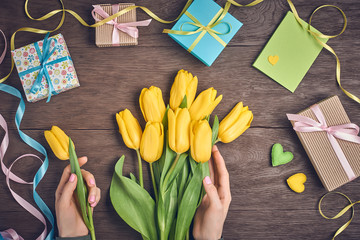 Female hands with tulips and gift box on wood 