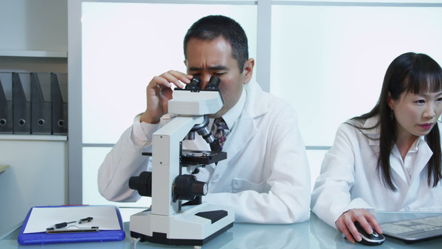 Scientists in lab work with microscope and computer