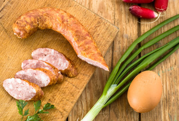 Piece of sausage and slices decorated with green parsley on wood