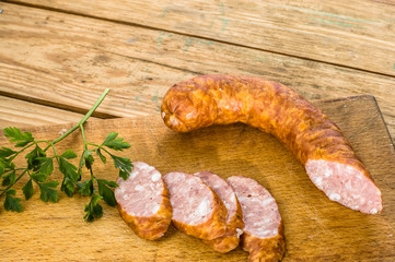 Piece of sausage and slices decorated with green parsley on wood