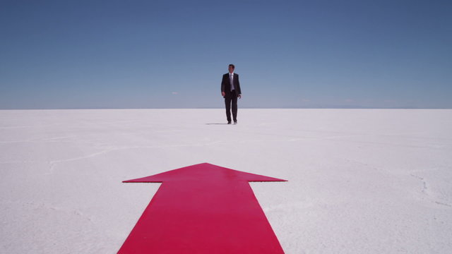 Businessman walks by red arrow at salt flat