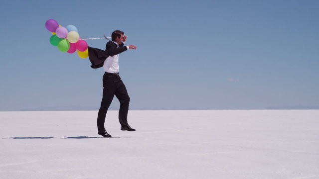 Businessman running with balloons at salt flat