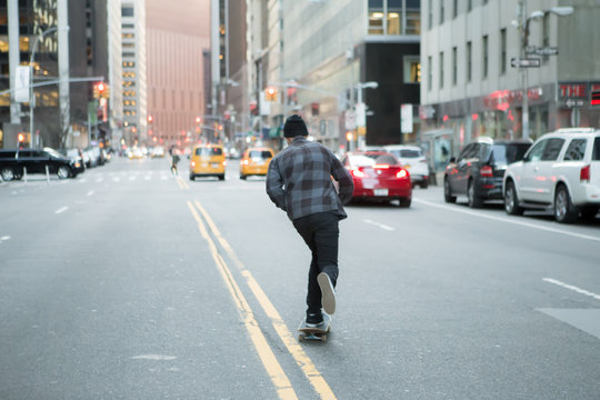 Back figure of young skateboarder cruising down the city street