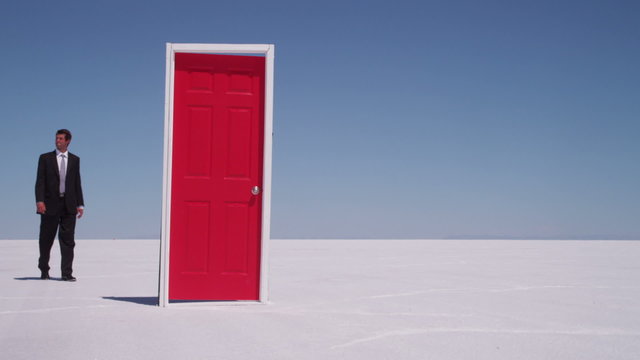 Businessman walks through red door at salt flat