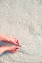 Fototapeta na wymiar Woman's feet on the white sand beach in shallow water