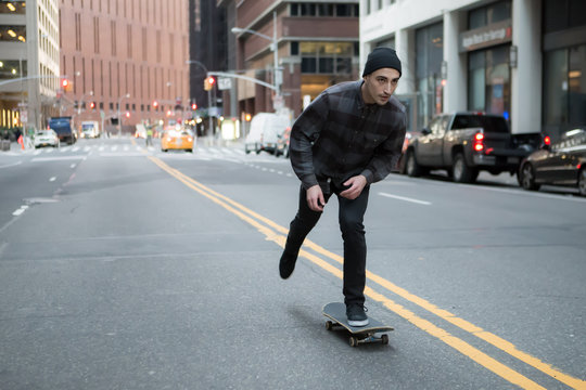 Young skateboarder cruising donw the city street before sunset.