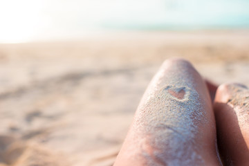 Female feet with heart drawing by sand