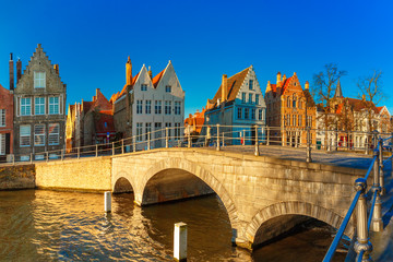 Obraz premium Malowniczy widok na kanał Brugii z pięknymi średniowiecznymi kolorowymi domami i słonecznym mostem rano, złota godzina, Belgia
