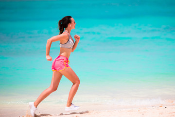 Fototapeta na wymiar Fit young woman running along tropical beach in her sportswear 