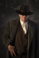 Sinister/Low key image of man in overcoat & hat in sinister pose with hand on gun against portrait...