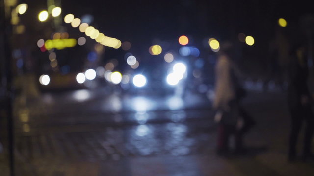 Slow motion footage of night traffic in a city center. Pedestrians cross the street on a crosswalk. Blurred image of people crossing the road.