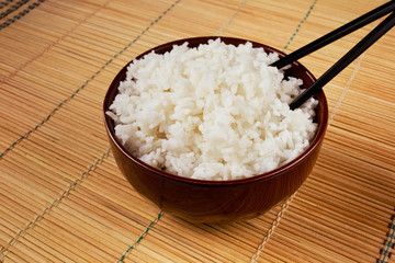 White rice in a bowl with chopsticks on a wooden mat
