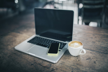 Blank cell phone on laptop and coffee mug on wooden table
