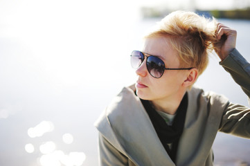 Young beautiful blonde girl sunbathing near the water. Wearing sunglasses. Outside