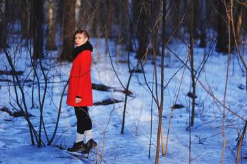 early spring portrait of cute attractive serious young girl with dark hair heat scarf and red jacket looking to camera and standing on wild forest natural background. Outdoor
