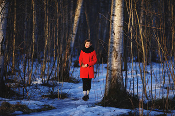 early spring portrait of cute attractive serious young girl with dark hair heat scarf and red jacket looking to sun and walking through the woods with a sprig in her hands. Outdoor