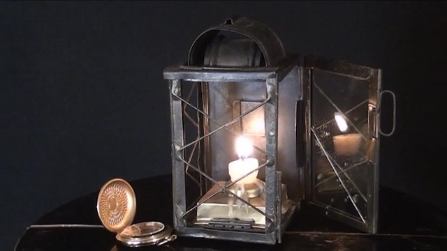 A candle burns in the old lamp, on a black background