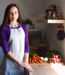Young woman standing in her kitchen near desk with shopping bags