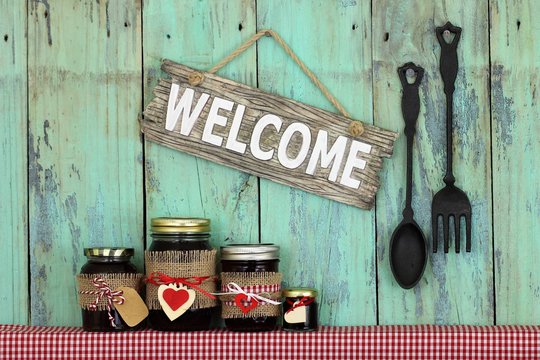 Welcome sign hanging by cast iron spoon and fork over jars of fruit jam