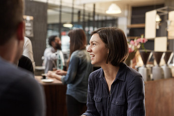 Brunette woman smiling and looking away in a busy cafe