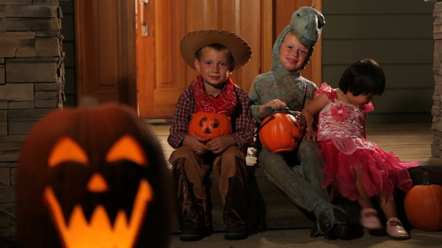 Portrait of three children in Halloween costumes sitting on porch