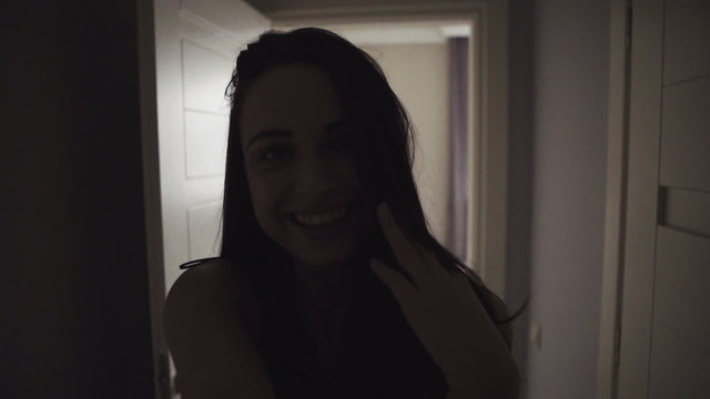 Young attractive happy woman runs through a hall in apartment and looking around,   then she comes into a bedroom and sits on a bed.  selfie shot.   