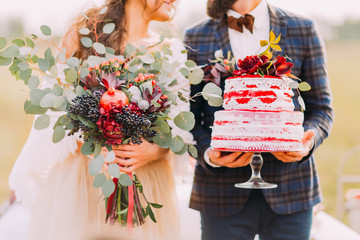 Wedding couple holds beautiful cake and bouquet close up