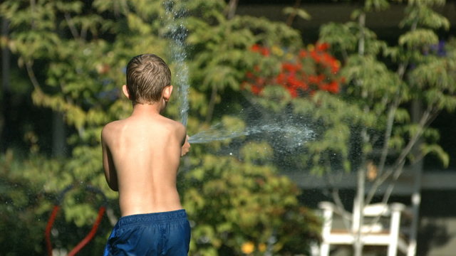 Kid spraying water from hose, slow motion