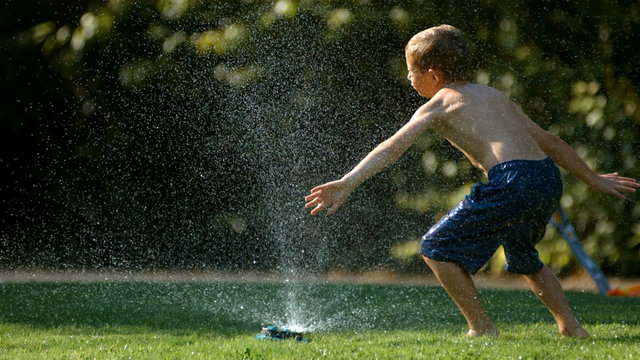 Child jumping in sprinkler, slow motion