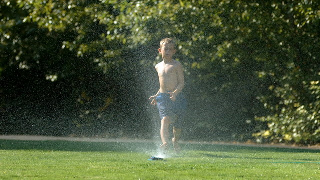 Kid jumping over sprinkler, slow motion