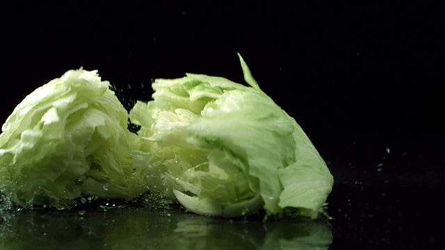 Head of lettuce splashing onto black reflective surface, slow motion