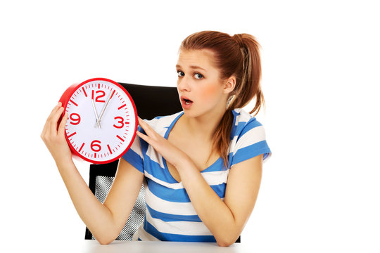 Young shocked teenage woman looking at clock