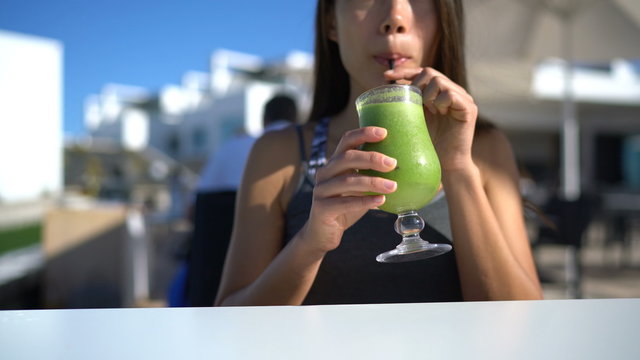 Green smoothie woman drinking healthy organic vegetable juice breakfast at restaurant cafe on outdoor terrace. Unrecognizable young adult taking a sip with straw eating vegetarian for a detox diet.