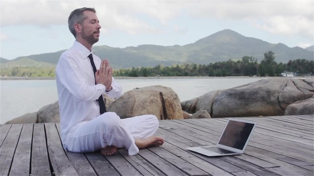 businessman doing yoga on a wooden bridge with a laptop
