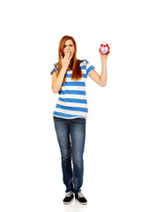 Yawning teenage woman holding alarm clock