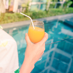 Rear view of beautiful woman in hat is holding orange juice glass in summer.