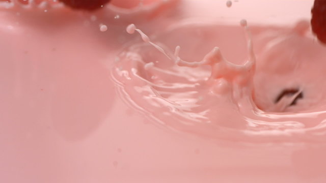 Raspberries splashing into pink cream, slow motion