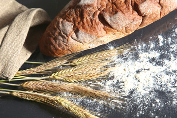 rustic crusty bread and wheat ears on a dark wooden table