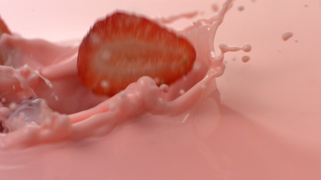 Fresh strawberries splashing into pink cream, slow motion