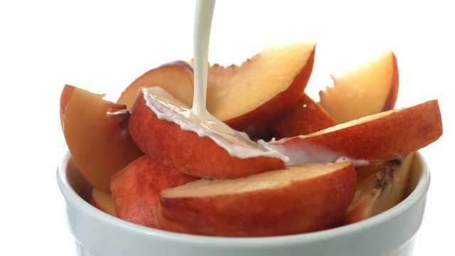 Pouring cream over bowl of fresh peaches, slow motion