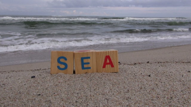 Word &ldquo;sea&rdquo; made out of letter cubes placed on sand beach by the sea