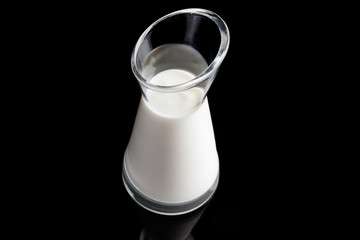 Glass pitcher with white yogurt on black background from above